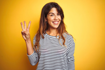 Young beautiful woman wearing stripes t-shirt standing over yelllow isolated background showing and...
