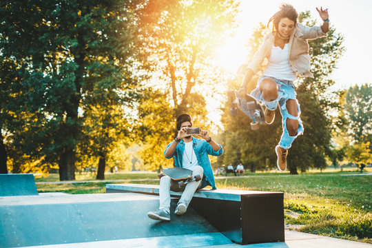 Beautiful young couple enjoying outdoors adn taking photos in city skateborading park