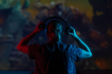 Girl gamer playing games in the headphones on a large screen, with bright light and a dark room.bright background