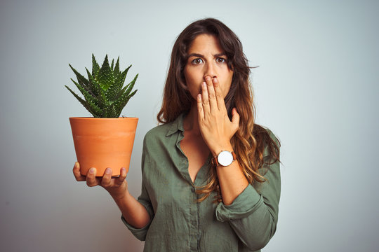 Young beautiful woman holding cactus pot over white isolated background cover mouth with hand shocked with shame for mistake, expression of fear, scared in silence, secret concept