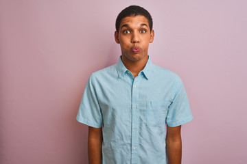Young handsome arab man wearing blue shirt standing over isolated pink background puffing cheeks...