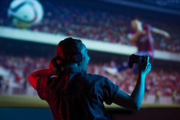 Soccer game, girl gamer playing a game in football headphones on a big screen, with bright light...