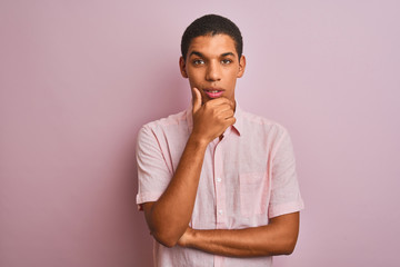 Young handsome arab man wearing casual shirt standing over isolated pink background looking confident at the camera with smile with crossed arms and hand raised on chin. Thinking positive.