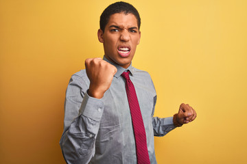 Young handsome arab businessman wearing shirt and tie over isolated yellow background angry and mad raising fist frustrated and furious while shouting with anger. Rage and aggressive concept.