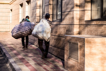 Homeless on the street with bags on their shoulders.