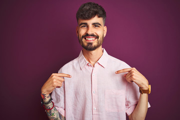 Young man with tattoo wearing summer pink shirt standing over isolated purple background looking...