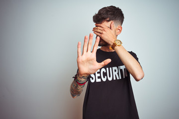 Young safeguard man with tattoo wering security uniform over isolated white background covering...