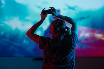 A gamer or a streamer girl at home in a dark room with a gamepad playing with friends on the networks in video games. A young man sits in front of a monitor