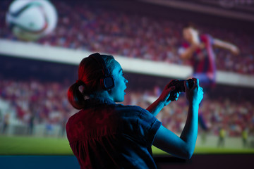 Fototapeta premium Soccer game, girl gamer playing a game in football headphones on a big screen, with bright light and a dark room. Gameplay, streaming, e-sports.