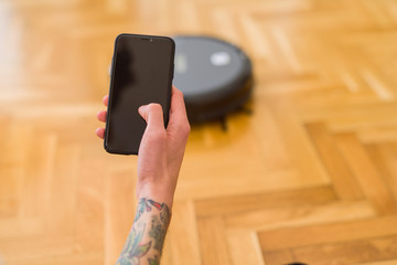 Close up of man hands controling automatic vacuum cleaner using electronic control of the mopping...
