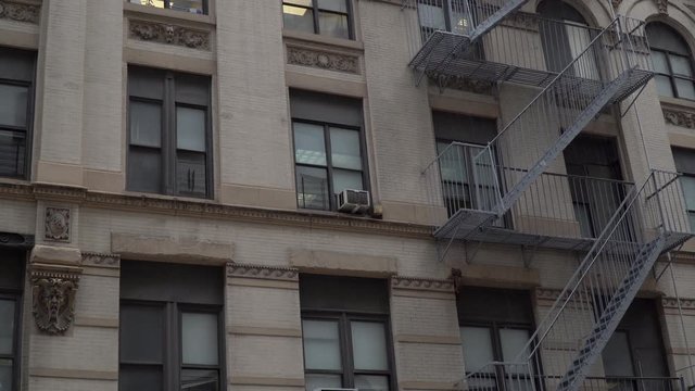 Day time establishing shot DX matching New York City style apartment building exterior. Window air conditioners and fire escape on facade structure construction view from street level