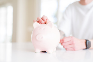 Close up of man putting a coin inside piggy bank as savings