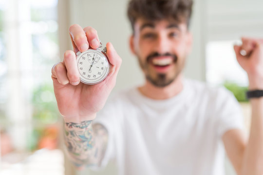 Young man using holding stopwatch screaming proud and celebrating victory and success very excited, cheering emotion