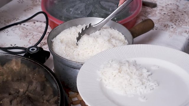 Person serving rice and other Brazilian food onto a plate