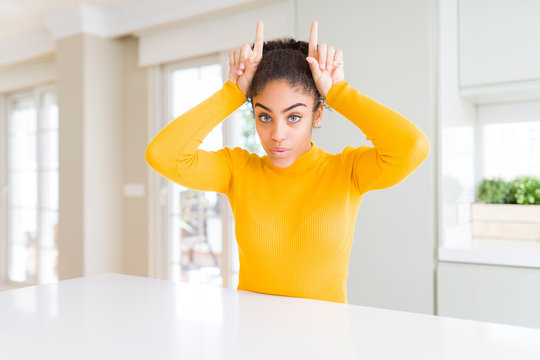 Beautiful african american woman with afro hair wearing a casual yellow sweater doing funny gesture with finger over head as bull horns