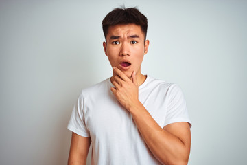 Young asian chinese man wearing t-shirt standing over isolated white background Looking fascinated with disbelief, surprise and amazed expression with hands on chin