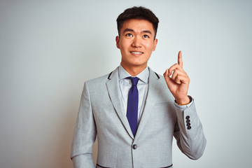 Asian chinese businessman wearing suit and tie standing over isolated yellow background pointing finger up with successful idea. Exited and happy. Number one.