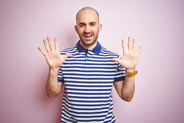 Young bald man with beard wearing casual striped blue t-shirt over pink isolated background showing and pointing up with fingers number ten while smiling confident and happy.