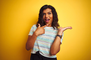 Beautiful transsexual transgender woman wearing t-shirt over isolated yellow background amazed and smiling to the camera while presenting with hand and pointing with finger.