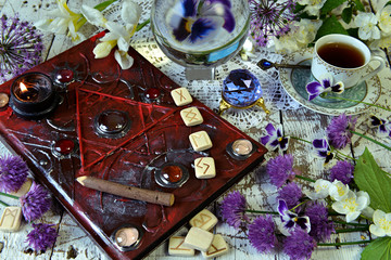 Magic book grimoire with runes, flowers, crystals and mystic objects on witch table.