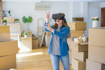 Fototapeta na wymiar Young blonde woman wearing virtual reality glasses playing a simulation game around cardboard boxes moving to a new house