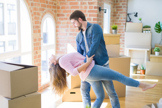 Young couple dancing celebrating moving to new apartment around cardboard boxes