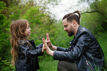 Modern stylish family walking in the park. Cute little daughter is calling dad to play. Time together. Family look. Urban casual outfit. Fatherhood makes life more livable