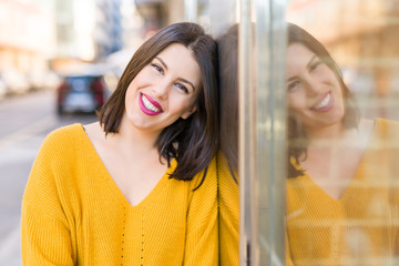 Beautiful young woman smiling confident and cheerful leaning on the wall, walking on the street of the city on a sunny day