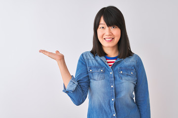 Young beautiful chinese woman wearing denim shirt over isolated white background smiling cheerful presenting and pointing with palm of hand looking at the camera.