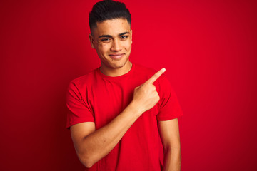 Young brazilian man wearing t-shirt standing over isolated red background Pointing with hand finger to the side showing advertisement, serious and calm face
