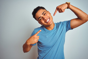 Fototapeta premium Young brazilian man wearing blue t-shirt standing over isolated white background smiling cheerful showing and pointing with fingers teeth and mouth. Dental health concept.