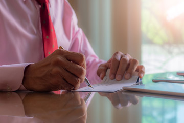 Businessman hand writing and signing a cheque with laptop computer on the desk.