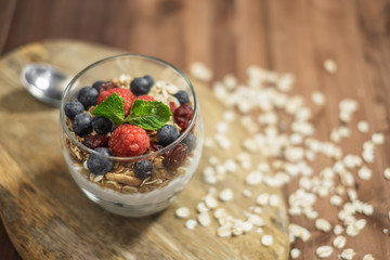 Healthy yogurt grain and berries dessert glass on top of a wooden tray on wood surface background.