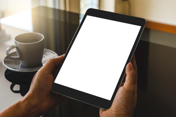Mockup image of hand holding and using black tablet pc computer  with isolated white screen with coffee cup on the office desk.  clipping path
