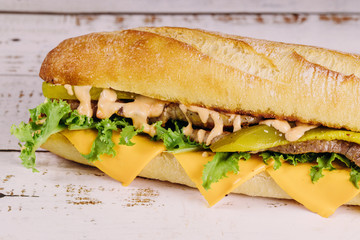 Sub sandwich with cheese and pickles on a white background.