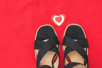 Summer fashion black women's shoes on red fabric with red heart. Flat lay.