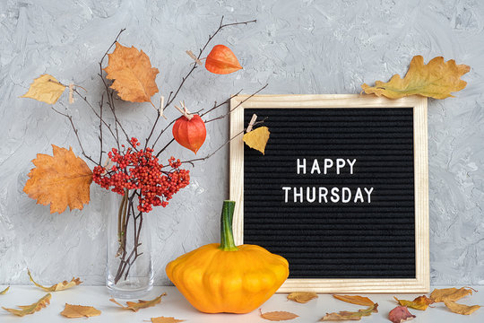 Happy Thursday text on black letter board and bouquet of branches with yellow leaves on clothespins in vase on table Template for postcard, greeting card Concept Hello autumn Thursday