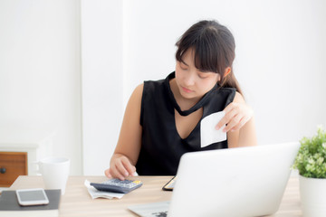 Beautiful young asian woman calculating expenses household and writing notebook on desk, girl checking bill and stress and note, female worry debt and tax, finance and business concept.