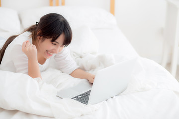 Beautiful portrait freelance asian young woman lying relax and leisure working laptop computer internet online on bed in bedroom, cheerful asia girl with gesture glad and success, lifestyle concept.