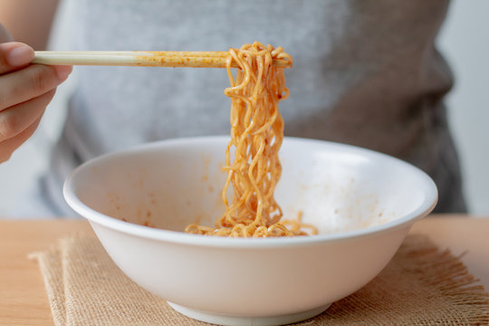 Woman eating instant noodle in white bowl.
