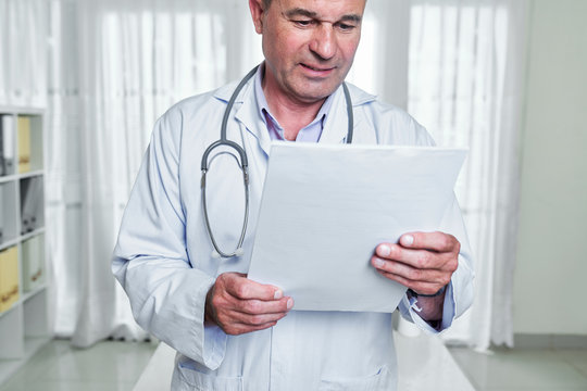 Frowning doctor in white labcoat reading medical history of patient