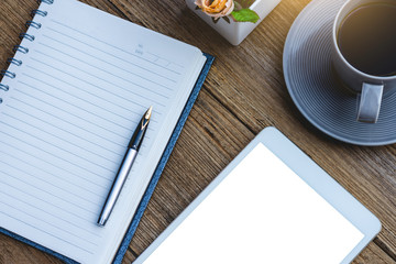 Mock up image of white digital tablet with blank screen,diary notebook, pen, cup of coffee and flowers on wooden table background. clipping path and copy space for your text, Top view