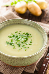 Fresh homemade cream of potato soup in bowl garnished with fresh chopped parsley, potatoes in the back (Selective Focus, Focus one third into the bowl)