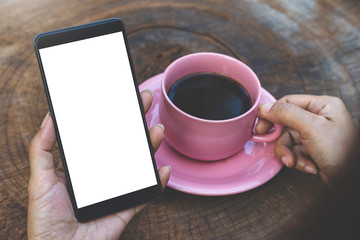 Mockup woman hand holding blank white screen mobile smart phone with cup of coffee on wood table.