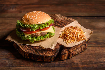 Tasty grilled homemade burgers with beef, tomato, cheese, cucumber and lettuce. Delicious grilled burgers. Craft beef burger and french fries on wooden table.