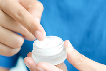 Hand of woman holding moisturizer cream and serum. She applying a facial cream , essential , oil , lotion and body cream for skin care, close up view and blur background. Beauty and Healthy Concept.