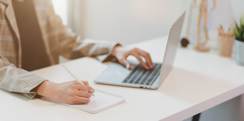 Fototapeta premium Businesswoman typing on laptop and writing on notebook