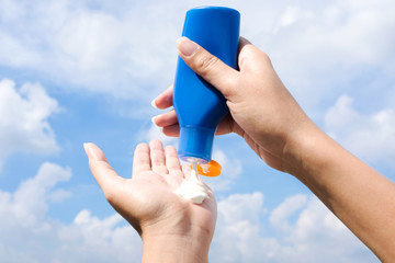 Hand of female holding sunscreen. Very sun light Sky background.Health concepts and skin care