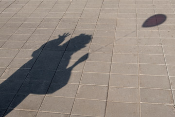 Shadow from a clown with a ball in his hand. Street pavement made of stone slabs. Copy space. Costume show or Halloween party.