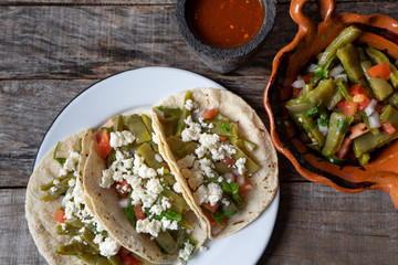 Mexican nopal cactus salad and tacos with cheese on wooden background